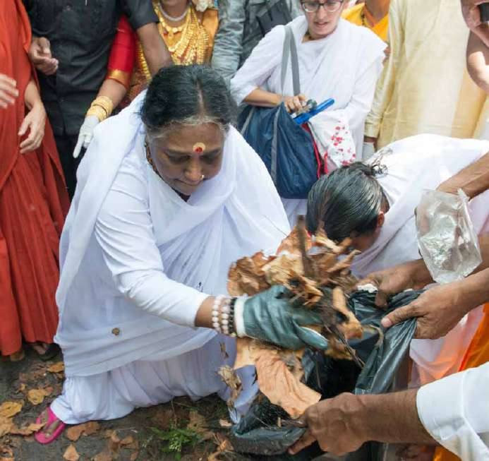 Amma bending to gather waste into a bag alongside volunteers